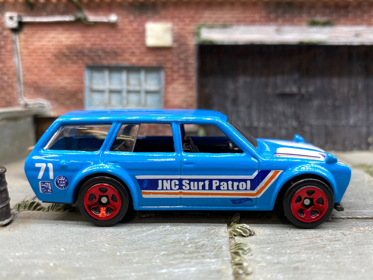 Vista lateral del Datsun 510 Wagon azul de Hot Wheels, con letras JNC Surf Patrol, número 71 y ruedas rojas