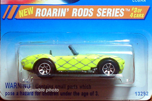 Hot Wheels Cobra amarillo con líneas grises cruzadas, en blíster transparente sobre tarjeta azul Roarin’ Rods marcada 3 de 4 y artículo 13292