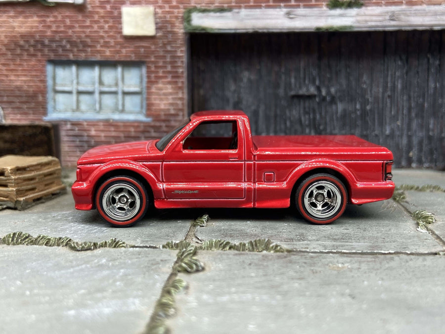 Red custom Hot Wheels GMC Syclone with chrome wheels and redline tires, viewed from the side