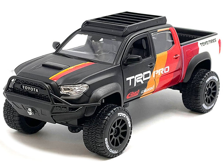 Matte black 2023 Toyota Tacoma TRD Pro off-road pickup with graphics and roof rack, unboxed front three-quarter view, Maisto 1:27.