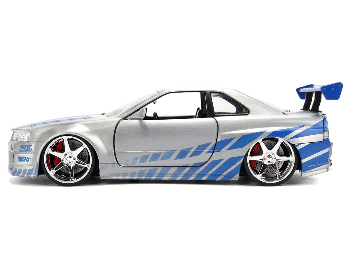Closed side profile of silver brush-finish Nissan Skyline R34 with blue graphics and rear wing, Jada 36818 in 1:24
