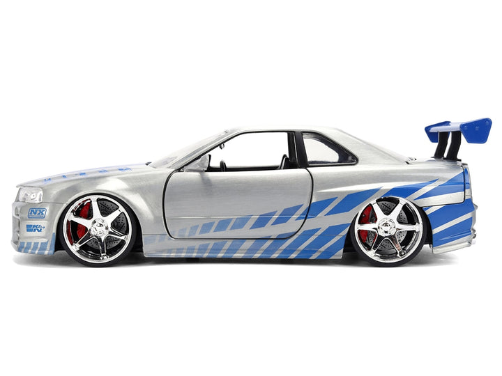 Closed side profile of silver brush-finish Nissan Skyline R34 with blue graphics and rear wing, Jada 36818 in 1:24