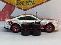 Chrome and red-lip wheels stacked in pairs, showing tire profiles and axle rods in front of a display car