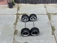 Overhead view of black and chrome 4-spoke wheels with black rubber tires positioned on axle rods