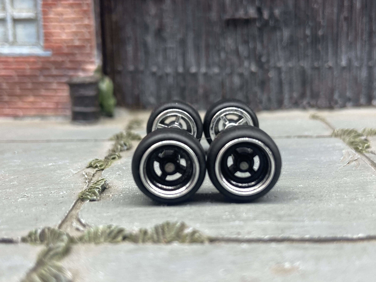 Front view of four 10mm black and chrome 4-spoke wheels with black rubber tires