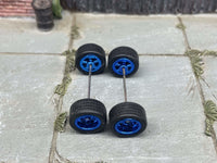 Overhead view of four blue anodized 5-star wheels with black rubber tires positioned on axle rods