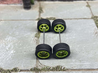 Overhead view of four green anodized 5-star wheels with black rubber tires positioned on axle rods