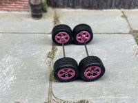 Overhead view of four pink anodized 5-star wheels with black rubber tires positioned on axle rods